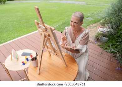 Woman Painting on an Easel Outdoors in a Garden Setting on a Wooden Deck - Powered by Shutterstock