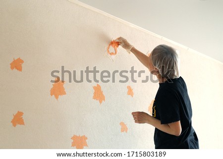 Woman painting the pattern on the wall with orange colour. Home renovation.