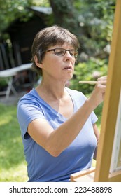 A Woman Painting A Picture In The Garden