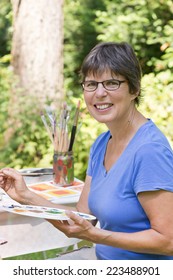 A Woman Painting A Picture In The Garden