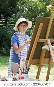 A Woman Painting A Picture In The Garden