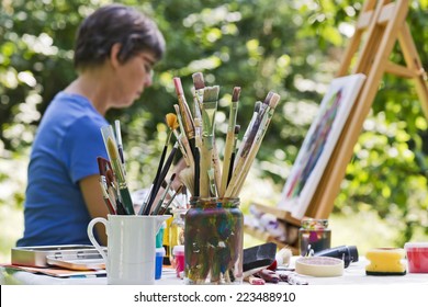 A Woman Painting A Picture In The Garden