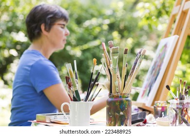 A Woman Painting A Picture In The Garden