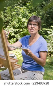 A Woman Painting A Picture In The Garden