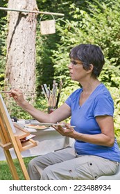 A Woman Painting A Picture In The Garden