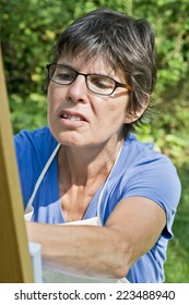 A Woman Painting A Picture In The Garden