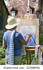 A Woman Painting A Picture In The Garden