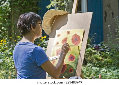 A Woman Painting A Picture In The Garden