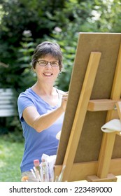 A Woman Painting A Picture In The Garden