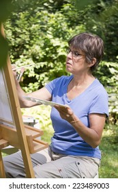 A Woman Painting A Picture In The Garden