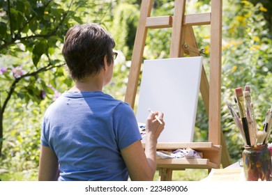 A Woman Painting A Picture In The Garden