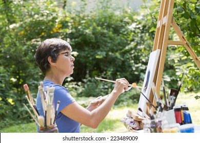 A Woman Painting A Picture In The Garden