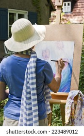 A Woman Painting A Picture In The Garden