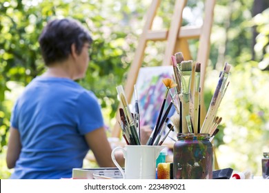 A Woman Painting A Picture In The Garden