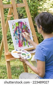 A Woman Painting A Picture In The Garden