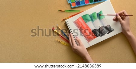 Woman painting UAE flag on beige background with space for text