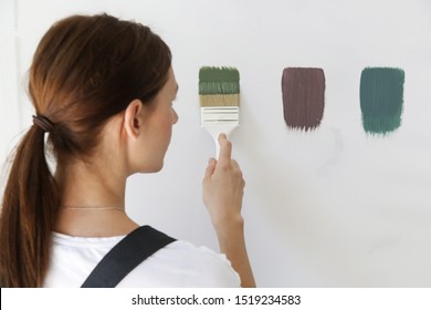 Woman Is Painting The Wall With Different Color Swatches. 
Process Of Choosing The Right Color For The Wall, DIY Home Improvement Concept. 