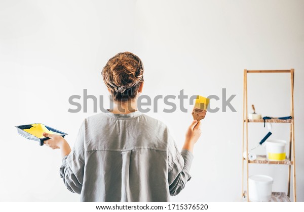 Woman painting wall.\
Rear view of woman with paint brush painting wall. Repair and house\
renovation concept.