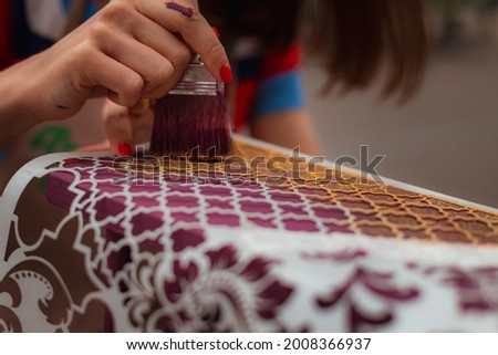 woman paints furniture with a brush on a stencil
