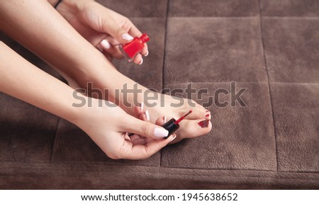 Woman paints her toenails with red pedicure.
