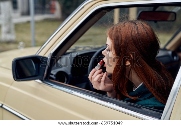  Woman paints lips, woman peeks out of car\
window                             \
