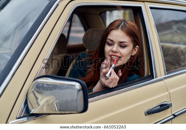    Woman paints lips, woman peeks out of car\
window                           \
