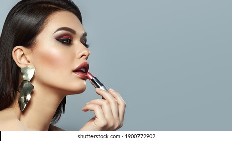 Woman paints lips with shiny lipstick. A dark-haired young woman with smooth skin and bright makeup posing in the studio.