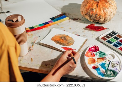 A woman paints picture and brush in sketchbook  Learning to draw at home  Autumn still life and pumpkin   red leaf  Creating content concept 