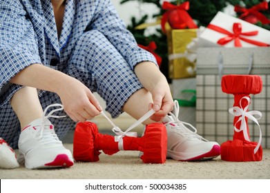 Woman In Pajamas And Athletic Shoes Unties The Bow On The Dumbbells. Christmas Present. Birthday Present.