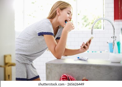 Woman In Pajamas Brushing Teeth And Using Mobile Phone