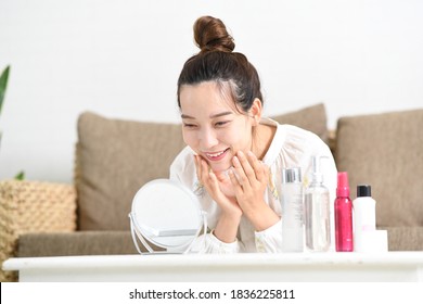 woman in pajamas and headband applying toner in front of the mirror.