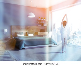 Woman in pajamas in interior of stylish loft bedroom with blue walls, wooden floor, green master bed and neat computer table in the corner. Toned image