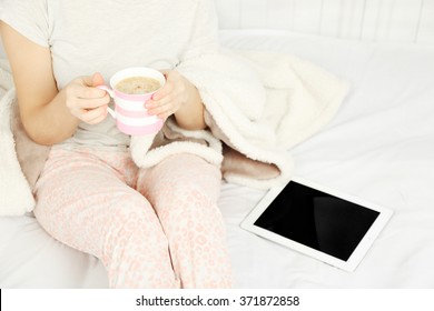 Woman In Pajamas With Tablet Drinking Coffee On Her Bed