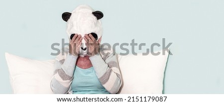 woman in panda mask sitting on bed. woman covering close her eyes with hands. middle aged woman with hand covering eyes