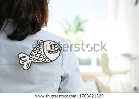 Woman with paper fish on back indoors, space for text. April fool's day