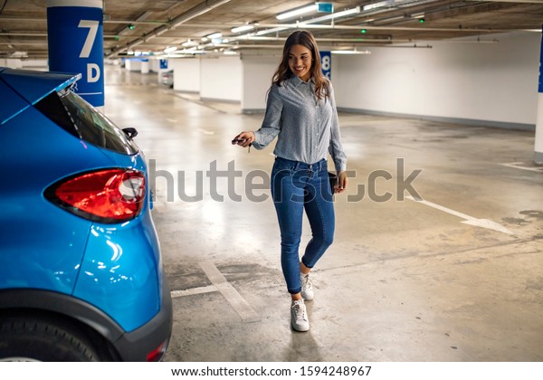 Woman in a parking garage, unlocking in her car.\
Woman activating her car alarm in an underground parking garage as\
she walks away. Business woman walking with car keys in the\
underground parking