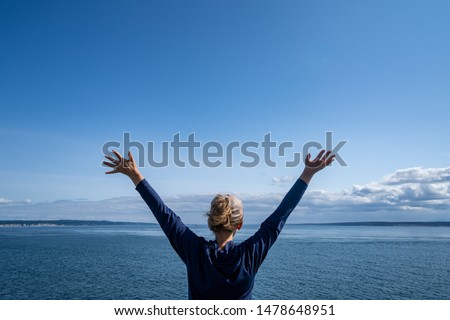 Woman passenger on the Port Townsend Ferry in Washington State stands with her arms up and back to the camera as the boat sails across Puget Sound