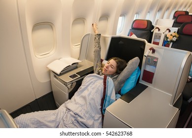 Woman Passenger Relaxing At The Business Class Of Airplane In Comfortable Single Seat. Flight At First Class Plane