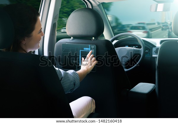 Woman passenger\
sitting in the backseat and  selects a route when her self-driving\
car rides on the highway.
