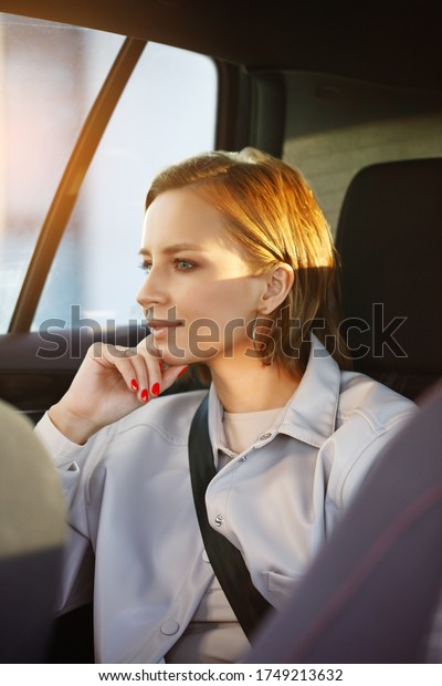 Woman passenger sitting on back seat of car with
comfort, in taxi or with personal driver, with sunlight of morning,
looking at window. 