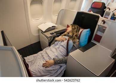 Woman Passenger Sleeping At The Business Class Of Airplane In Comfortable Single Seat. Flight At First Class Plane