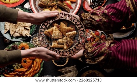 A woman passes a plate of fried samosa to a man. Dinner together. Authentic local homemade traditional meals in traditional dishes