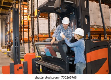 Woman Passing Note To Forklift Driver In Warehouse