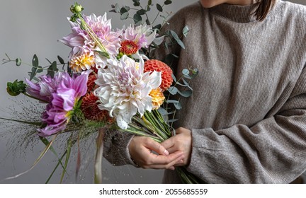 A woman in a pastel sweater holds a festive bouquet of chrysathemum flowers in her hands.