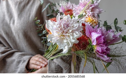 A woman in a pastel sweater holds a festive bouquet of chrysathemum flowers in her hands.