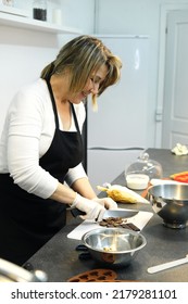 A Woman Pastry Chef In A Black Apron Cuts A Bar Of Hot Chocolate To Use For Making Dessert. Vertical Photo