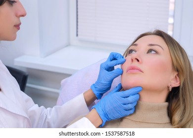 Woman patient is consulted by a cosmetologist before rejuvenating injections into the face. Young doctor talking with woman, examine and chekup her face. Preparing to beauty procedure in clinic.
