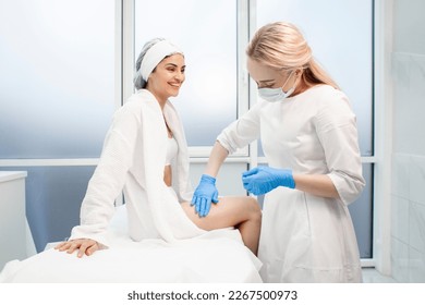 woman patient with cosmetologist doctor in cosmetology office, cosmetologist doctor applies cream on girl's leg, leg epilation procedure, leg skin care - Shutterstock ID 2267500973