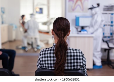 Woman Patient In Dentistiry Office Waiting For Diagnosis In Dental Clinic Corridor. Dentist And Staff Dressed In Ppe Suit Consulting Patient. Filling Health Form.