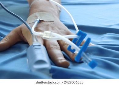 Woman patient in he bed with IV acess an pulse oximeter sensor in the hand. Close up of a intravenous infusion connector